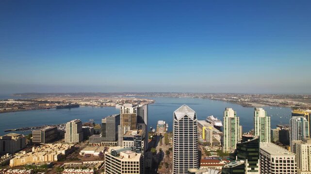 Drone flying backward above downtown San Diego at 9AM facing the harbor with camera slowly tilting down to reveal streets below repass.