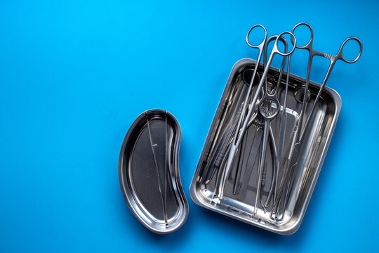 Sterile surgical instruments and tools - scalpels, scissors and others - in a stainless tray on blue background, top view