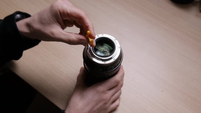 Close-up of hands unscrewing the mount on a cinema lens to swap from EF to PL bayonet. Detailed lens modification process shown on a wooden desk. Real hands-on camera gear footage.