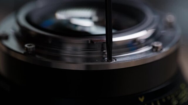 Low angle side view of hands removing a Torx screw from a cinema lens mount during EF to PL conversion. Screwdriver and lens body clearly visible. Detailed technical modification footage.