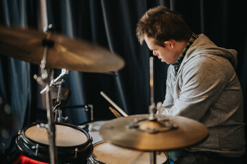 Obraz premium A male drummer practices on a drum kit, concentrating on his playing. The focused student musician rehearses in a dim studio setting.