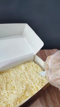 Close up of a hand holding layered milk brownies topped with shredded cheese in a clean background setting. The video shows cutting the cake to reveal soft moist texture.