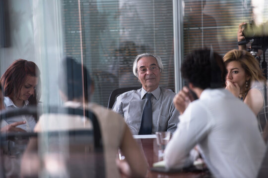 Senior executive leading a business meeting in a modern glass boardroom with attentive team members