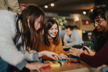 A group of students and friends play with colorful wooden blocks and smile together. The casual indoor scene shows young adults enjoying a cooperative tabletop game and social time. © qunica.com