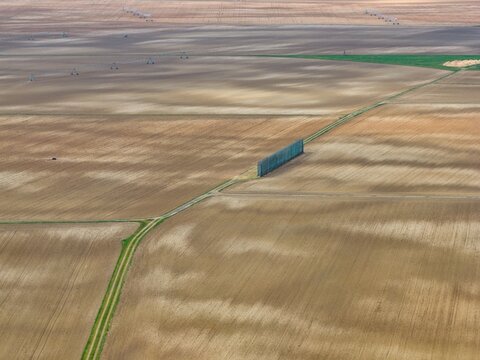 Aerial view of a dirt road cutting through vast, patterned fields, creating a stark contrast between the natural earth tones and the linear path, Neuf-Brisach, Grand Est, France.