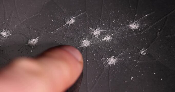 thin broken glass on black paper, dents and dots on the glass where it broke, cracks and completely broken places on the glass on a black uneven background