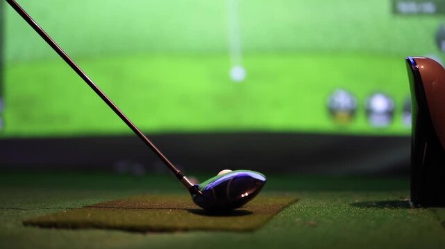 Slow motion shot of golfer hitting ball with driver in indoor golf simulator facility.