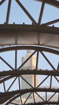 A stunning view of the Makkah Royal Clock Tower rising majestically between modern high-rise buildings in Mecca, Saudi Arabia. The iconic clock face stands tall against the sky, symbolizing Islamic he