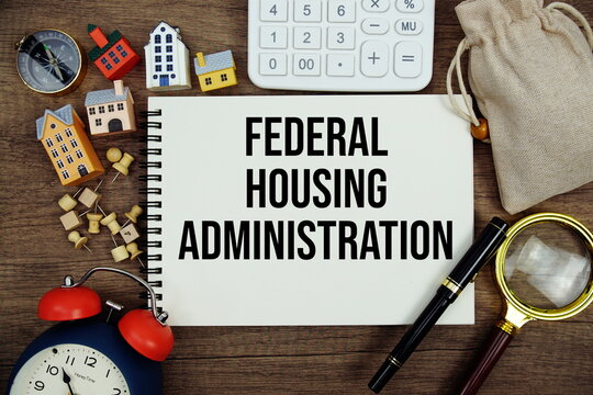 Federal Housing Administration text written on notepad with house model, magnifying glass, alarm clock and calculator on wooden background
