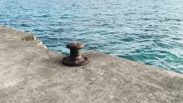 Rusty mooring bollard on a concrete dock by the sea with choppy water