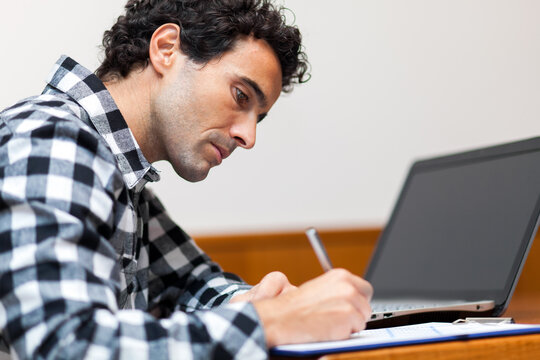 Man concentrating on work at laptop with notebook