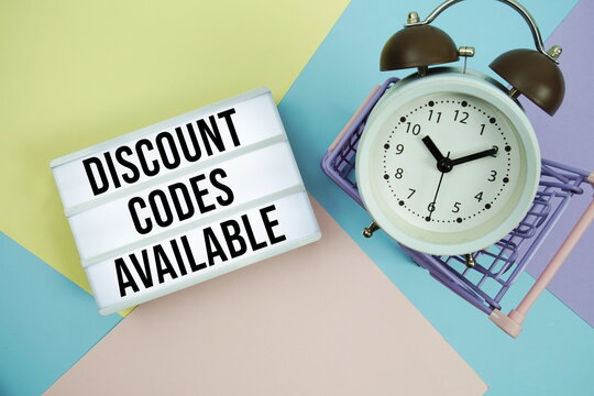 Discount Codes Available text in lightbox with trolley shopping cart and alarm clock flat lay on multicolor pastel background