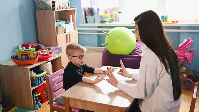 female therapist and boy practicing hand gestures in therapy session, concept of child development and alternative communication