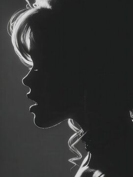Dramatic black and white silhouette of a woman in profile with backlit hair and soft rim lighting against a dark background