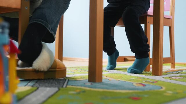 Bottom view of a child's legs sitting on a high chair in kindergarten