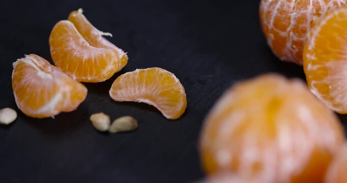 sliced juicy peeled orange tangerine on a black table, ripe orange small mandarin without peel on a black slate board, tangerine divided into small slices