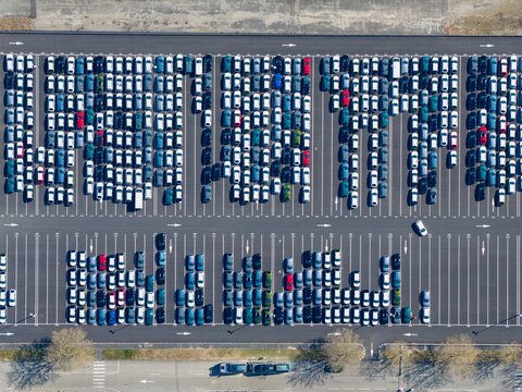 Aerial view of hundreds of cars neatly arranged in a vast parking lot, showcasing a symphony of colors and geometric precision, Sausheim, Grand Est, France.