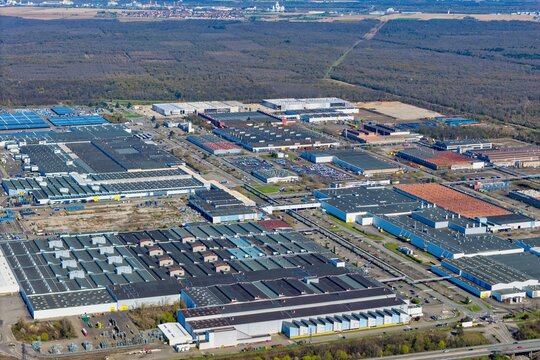 Aerial view of sprawling industrial complex meeting the edge of a dense forest under a vast sky, a symphony of human endeavor and natural tranquility, Sausheim, Grand Est, France.