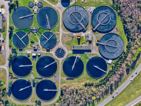 Aerial view of circular water treatment tanks reflecting the sky, contrasted by the surrounding verdant landscape, Sausheim, Grand Est, France.