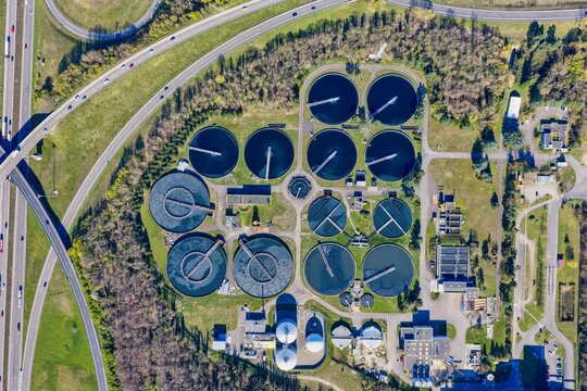 Aerial view of circular wastewater treatment pools contrasting with the linear highway and surrounding lush greenery, Sausheim, Grand Est, France.