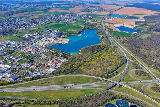 Aerial view of the vibrant blue waters of a quarry lake contrasting with the surrounding industrial area and lush greenery, Sausheim, Grand Est, France.