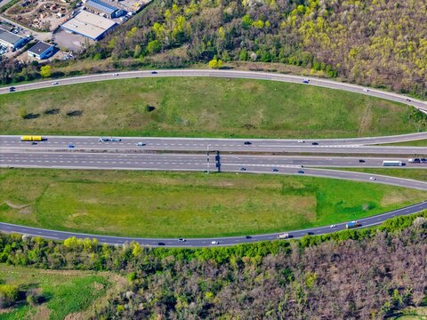 Aerial view of a vibrant highway bisecting verdant fields, framed by an oval of lush greenery and scattered trees, Sausheim, Grand Est, France.