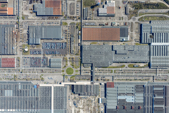 Aerial view of industrial rooftops and organised parking spaces create a geometric puzzle of textures and tones, contrasting with small patches of green, Sausheim, Grand Est, France.