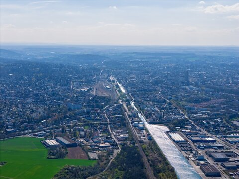 Aerial view of the glimmering canal cutting through the urban sprawl near the industrial zone and lush fields, Sausheim, Grand Est, France.