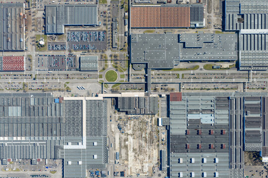 Aerial view of vast industrial rooftops casting shadows, a symphony of geometric shapes and textures, with a roundabout providing a touch of green amidst the concrete, Sausheim, Grand Est, France.