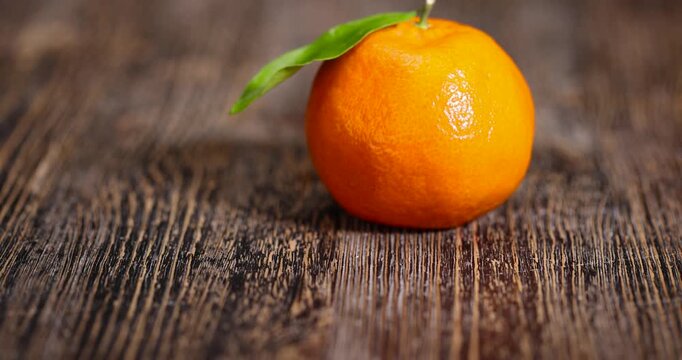 ripe orange tangerine with one green leaf, fruit on a wooden table, unpeeled ripe orange-skinned small tangerine with a long green leaf