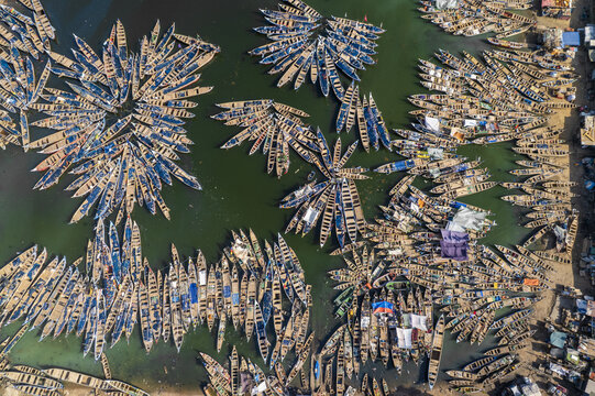 Aerial view of wooden boats clustered like petals on the water's surface, creating floral patterns of brown against the dark green, Tema, Ghana.