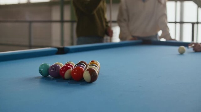 Close up shot of billiard balls rolling and scattering across blue pool table after break shot, unrecognizable players blurred in background