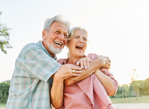 Happy active senior couple having fun talking and hugging in park outdoors