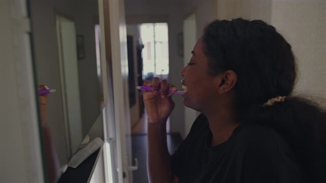 African American woman brushing teeth while facing bathroom mirror as part of daily morning routine creating simple and focused hygiene moment in home environment