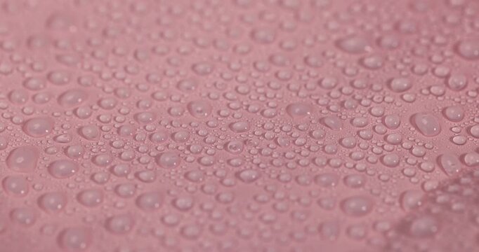 The plastic is covered with water, a pink plastic film with numerous small droplets and moisture on the surface in soft light with clear details and organic texture.