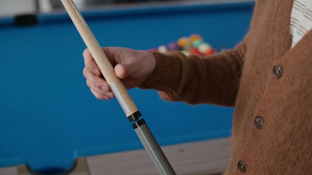 Side view closeup shot of unrecognizable player twisting cue stick with blue pool table and colorful billiard balls scattering from triangle blurred in background, preparing for game