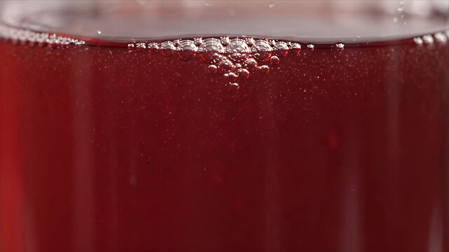Close up of red kombucha pouring into glass with bubbles in macro view. Red Sparkling Drink, Glass, Bubbles