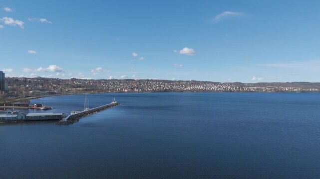 Aerial view of Torquay Harbour in Devon England with long pier extending into calm bay, hillside town in background under clear blue sky, scenic coastal landscape