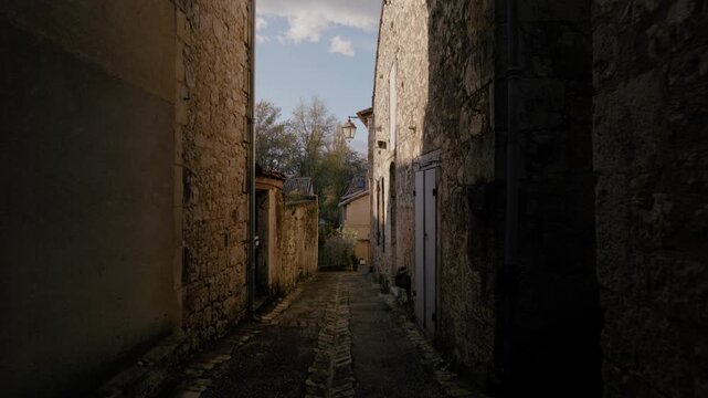 Stone buildings and wooden shutters line a narrow cobblestone street in the historic Bastide d'Issigeac, Dordogne department, France. A lantern hangs from a masonry wall.