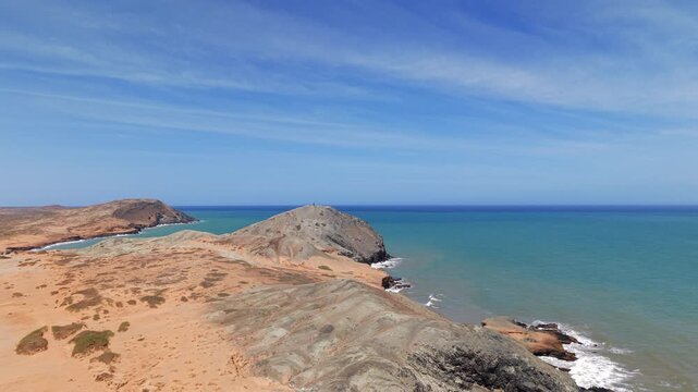 Experience a breathtaking aerial view of Pilon de Azucar in Cabo de la Vela, showcasing striking rock formations, turquoise sea, and expansive sky under vivid sunshine.