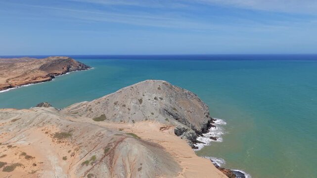 Breathtaking aerial footage of Pilon de Azucar, Cabo de la Vela, showcasing rugged coastal terrain and turquoise waters under a clear blue sky. Ideal for travel and nature visuals.