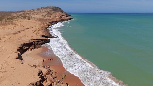 Breathtaking aerial footage over Playa Dorada in La Guajira, Colombia. Observe rugged cliffs and turquoise waters as waves gently kiss the untouched sandy beach.