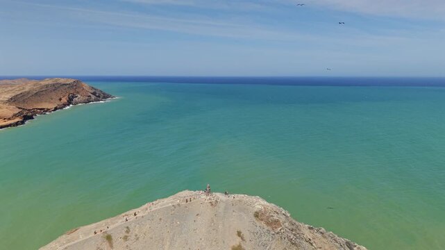 Stunning aerial footage captures Pilon de Azucar in Cabo de la Vela, Colombia, showcasing vibrant blue ocean and rugged landscape under a clear sky. Perfect for showcasing natural beauty.