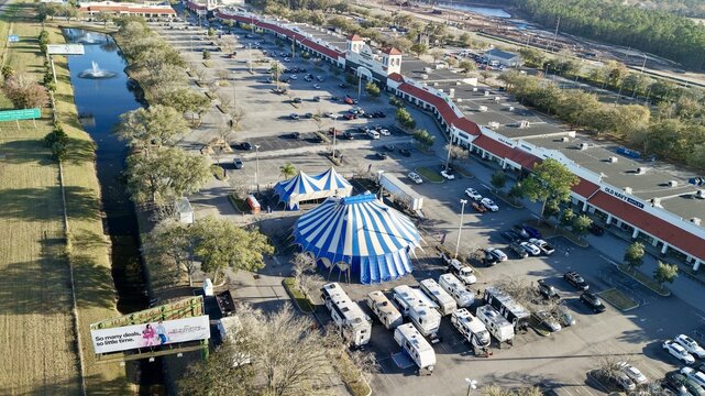 Aerial view of blue and white striped circus tents contrasting against the vast parking lot and red-roofed outlets near the World Golf Village, St. Augustine, Florida, United States.