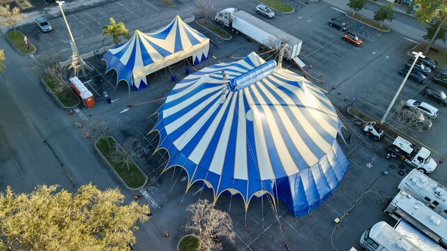 Aerial view of the vibrant blue and white striped circus tents standing boldly amidst the stark asphalt of the parking lot, St. Augustine, Florida, United States.