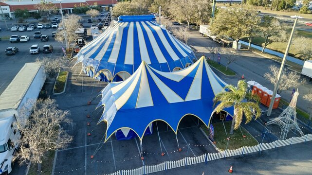 Aerial view of striking blue and white striped circus tents standing boldly against the neutral-toned parking lot, a vibrant spectacle under the Florida sun, St. Augustine, Florida, United States.