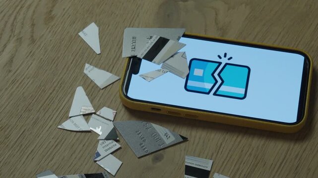 Hand holding pieces of a destroyed credit card next to a smartphone displaying an error symbol. Concept of payment failure, financial problem, and digital transaction issues.