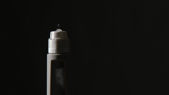 Black isolated close-up: Medication squirts from medical injection pen