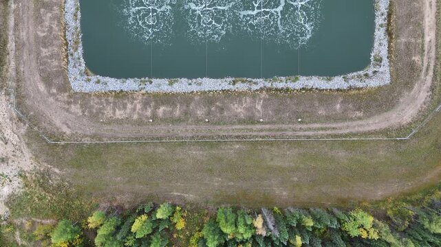 Aerial drone flies top-down forward over wastewater lagoons near Ilford War Lake, northern Manitoba, Canada. Aeration bubbles, berms, gravel road, and surrounding boreal forest visible.