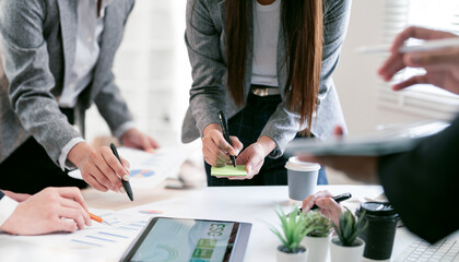 Diverse business team collaborating at office desk, analyzing ESG reports and financial charts while brainstorming with sticky notes.